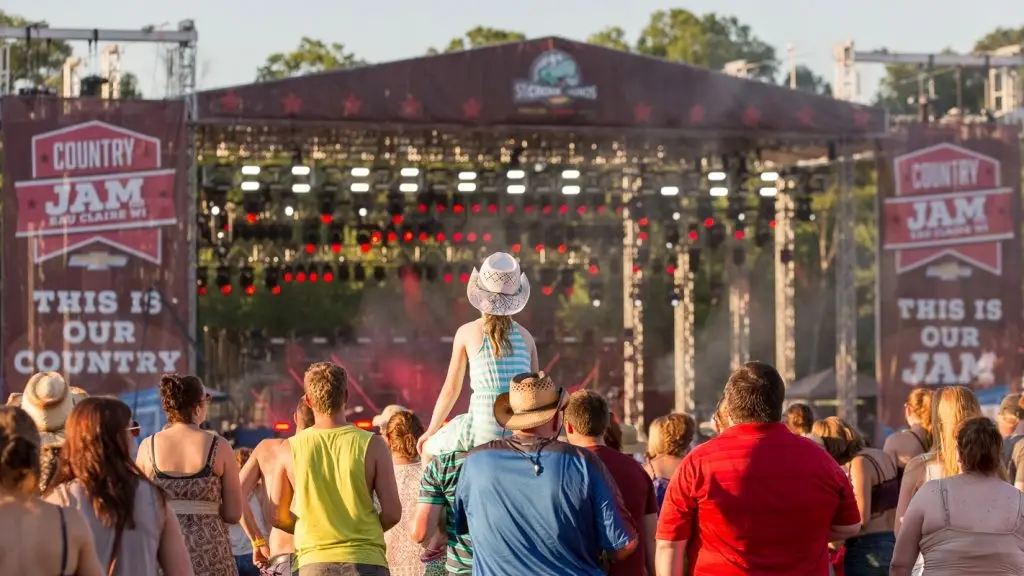 A crowd of people standing around in front of an outdoor stage.